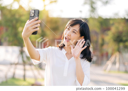 Portrait beautiful young asian woman with smart mobile phone around outdoor nature view in a sunny summer day Portrait beautiful young asian woman with smart mobile phone around outdoor nature view in a sunny summer day 100041299