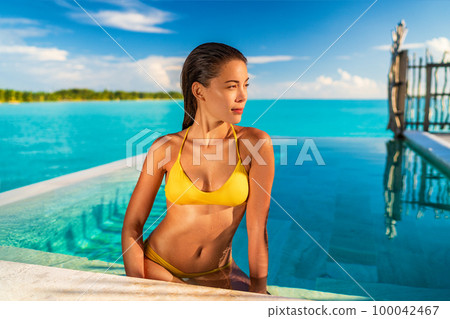 Luxury swimming pool Asian bikini model woman wearing yellow fashion swimsuit relaxing in infinity pool at overwater bungalow resort, tropical vacation Luxury swimming pool Asian bikini model woman wearing yellow fashion swimsuit relaxing in infinity pool at overwater bungalow resort, tropical vacation 100042467