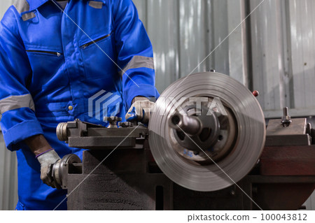 Engineering worker man wearing uniform safety working machine lathe metal brake disc grinder. 100043812