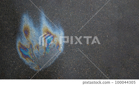 Iridescent spot of gasoline. Petrol on the asphalt a big polluted puddle water. A rainbow slick of gasoline Iridescent spot of gasoline. Petrol on the asphalt a big polluted puddle water. A rainbow slick of gasoline 100044305