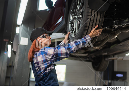 Female mechanic adjusting the tire of the car that is on the lift. A girl at a man's work. Female mechanic adjusting the tire of the car that is on the lift. A girl at a man's work. 100046644