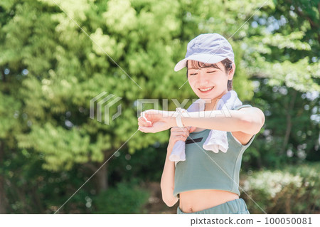 一位女士在公園裡邊看手錶邊鍛煉、訓練和散步（時間、時間、醫療保健） 100050081