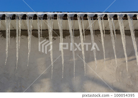 Sharp icicles and melted snow hanging from the eaves of the roof. Beautiful transparent icicles slowly gliding of a roof Sharp icicles and melted snow hanging from the eaves of the roof. Beautiful transparent icicles slowly gliding of a roof 100054395