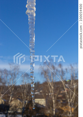 Icicles hang on the roof of a house against a bright blue sky. Spring landscape with icicles hanging from the roof of the house. Set of snow icicles, snow hat Icicles hang on the roof of a house against a bright blue sky. Spring landscape with icicles hanging from the roof of the house. Set of snow icicles, snow hat 100054400