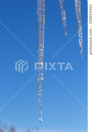 Sharp icicles and melted snow hanging from eaves of roof. Beautiful transparent icicles slowly gliding of a roof Sharp icicles and melted snow hanging from eaves of roof. Beautiful transparent icicles slowly gliding of a roof 100054402