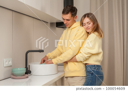 Happy couple in yellow clothes laughing hugging and washing the dishes Happy couple in yellow clothes laughing hugging and washing the dishes 100054609