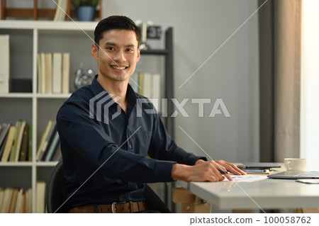 Elegant asian businessman sitting in front of laptop and looking confidently to camera 100058762
