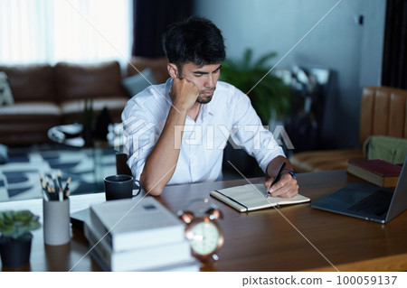 Portrait of an Asian man using a computer and note book to record his work. 100059137