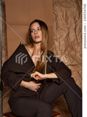 Tenderness. Studio portrait of young beautiful girl with blonde straight hair, in stylish dark suit posing against light brown background. Concept of beauty and fashion Tenderness. Studio portrait of young beautiful girl with blonde straight hair, in stylish dark suit posing against light brown background. Concept of beauty and fashion 100059706