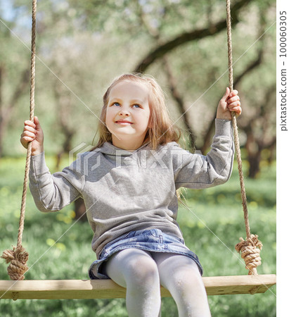 smiling little girl sitting on a swing in the garden 100060305