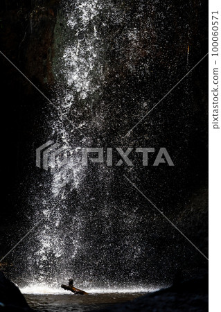 Splashing waterfall drop on pond with dark background of cave. 100060571