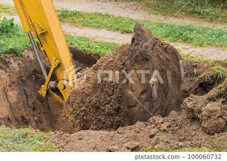 Excavator bucket with a pile of earth digs a large deep hole in the industrial area of the construction site Excavator bucket with a pile of earth digs a large deep hole in the industrial area of the construction site 100060732