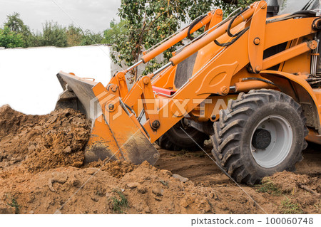 A bucket of a bulldozer fills the trench with earth in an industrial zone 100060748