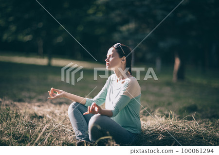 beautiful young woman meditating in Lotus position sitting on the lawn. 100061294