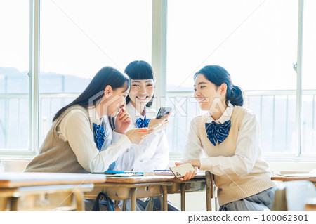 A high school student talking to his classmate while looking at his smartphone in the classroom 100062301