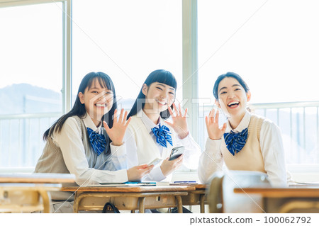 A high school student talking to his classmate while looking at his smartphone in the classroom 100062792