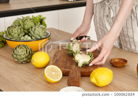 Woman cooking green artichokes in the kitchen Woman cooking green artichokes in the kitchen 100062884