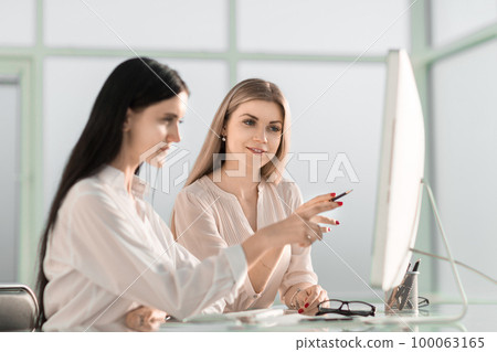 two employees are discussing something sitting at the office table 100063165