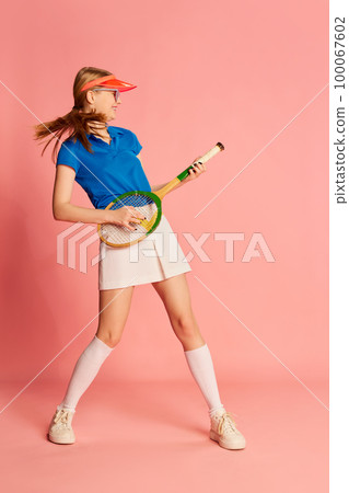 Playing racket like guitar. Fun. Portrait of beautiful young girl in sportive clothes posing with tennis racket over pink background. Concept of emotions and sportive lifestyle 100067602
