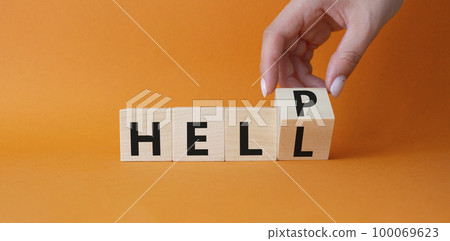 Help vs Hell symbol. Businessman hand Turnes cube and changes word Hell to Help. Beautiful orange background. Psychology and Help vs Hell concept. Copy space 100069623
