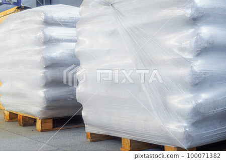 Storage of packaged goods or cargo in warehouse. On wooden pallets there are bags of cement wrapped 100071382