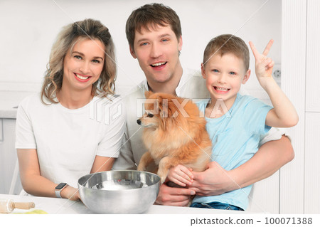 Cheerful happy family of three together with Spitz dog sit at kitchen table and laugh. Portrait of 100071388