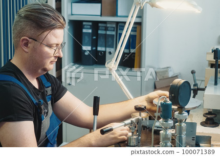 Professional calibration of pressure gauges and sensors. Working person sits at desk and is engaged Professional calibration of pressure gauges and sensors. Working person sits at desk and is engaged 100071389