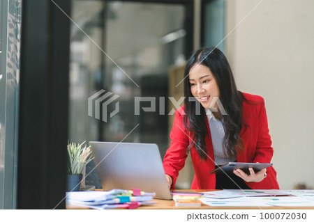 A beautiful Asian businesswoman is using a digital laptop at her desk in a modern office. A beautiful Asian businesswoman is using a digital laptop at her desk in a modern office. 100072030