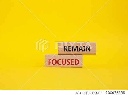 Remain focused symbol. Concept words Remain focused on wooden blocks. Beautiful yellow background. Business and Remain focused concept. Copy space. 100072368