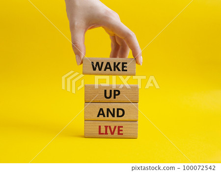 Wake up and live symbol. Wooden blocks with words Wake up and live. Beautiful yellow background. Businessman hand. Business and Wake up and live concept. Copy space. 100072542