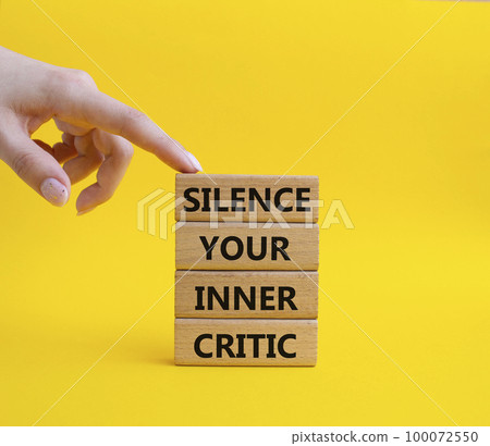 Silence your inner critic symbol. Wooden blocks with words Silence your inner critic. Beautiful yellow background. Businessman hand. Business and Silence your inner critic concept. Copy space. 100072550