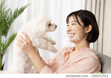 Woman sitting on a sofa and hugging a dog with a smile 100072561