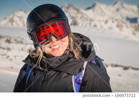 skier smiles in a safety ski helmet and goggles against the backdrop of the picturesque Alpine mountains. Active sports people and success concept image 100073722