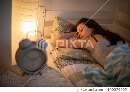A woman with a slight smile sleeps on her stomach in her bed. A woman with a slight smile sleeps on her stomach in her bed. 100074065