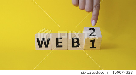 WEB 2 or 1 symbol. Businessman hand points at turned wooden cubes with words WEB 1 and WEB 2. Beautiful yellow background. Business and WEB concept. Copy space 100074328