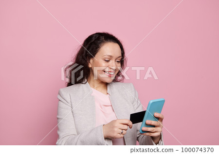 Smiling woman, bank client using smartphone and credit card, pays bills, making purchase online, booking tours hotels via mobile apps, enjoys the internet banking service, isolated on pink background Smiling woman, bank client using smartphone and credit card, pays bills, making purchase online, booking tours hotels via mobile apps, enjoys the internet banking service, isolated on pink background 100074370