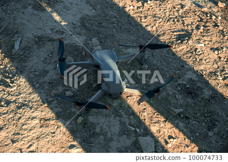 Drone Lies On Sand With Rocks In Shadow Of Man In Golden Hour. 100074733