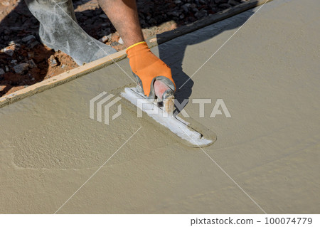 An employee plasters wet concrete cement floor using trowel after concrete has just been poured 100074779