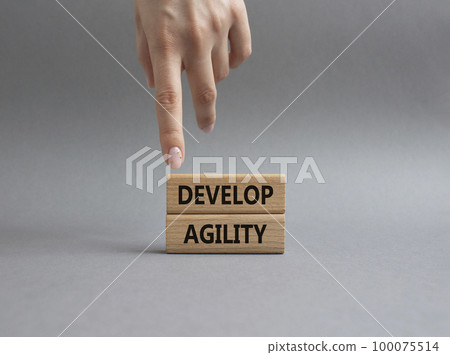 Develop agility symbol. Concept word Develop agility on wooden blocks. Beautiful grey background. Businessman hand. Business and Develop agility concept. Copy space Develop agility symbol. Concept word Develop agility on wooden blocks. Beautiful grey background. Businessman hand. Business and Develop agility concept. Copy space 100075514