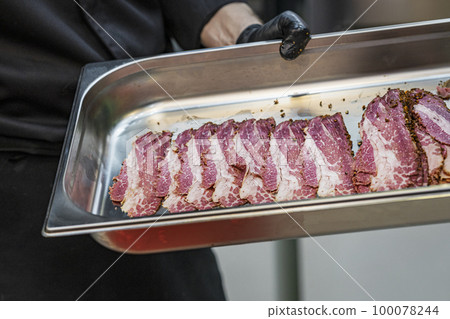 Metal dish in hand of cook with sliced pieces of meat Metal dish in hand of cook with sliced pieces of meat 100078244