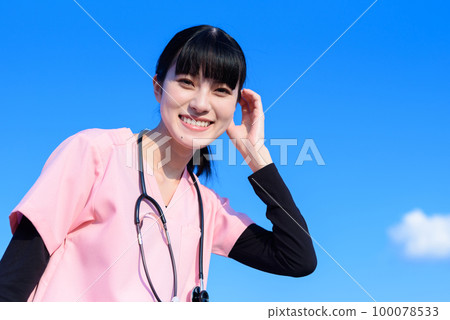A female nurse wearing a scrub standing against the blue sky, a medical worker, a doctor, a caregiver, an examination, brushing her hair 100078533
