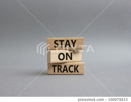 Stay on track symbol. Wooden blocks with words 'Stay on track'. Beautiful yellow background. Businessman hand. Business and 'Stay on track' concept. Copy space. Stay on track symbol. Wooden blocks with words 'Stay on track'. Beautiful yellow background. Businessman hand. Business and 'Stay on track' concept. Copy space. 100078815