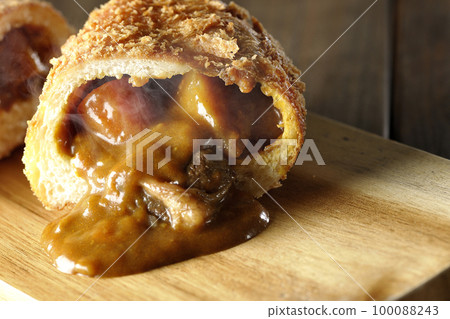 Hot curry bread with vegetables and beef that is cut in half on a cutting board and the roux flows out 100088243