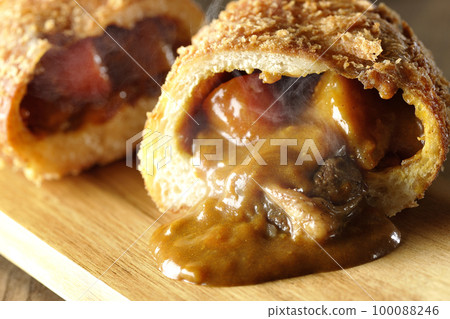Hot curry bread with vegetables and beef that is cut in half on a cutting board and the roux flows out 100088246