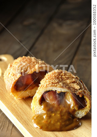 Hot curry bread cut in half on a cutting board with roux flowing out Hot curry bread cut in half on a cutting board with roux flowing out 100088352