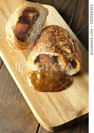 Hot curry bread cut in half on a cutting board with roux flowing out 100088363