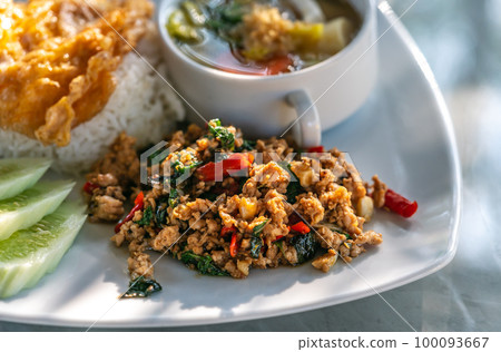 Thai classic spicy menu, Moo Pad Kaprow, or stir-fried ground pork with basil with white rice. Pork basil on a white plate with a Thai omelet over jasmine rice, vegetable soup, and sliced cucumbers. Thai classic spicy menu, Moo Pad Kaprow, or stir-fried ground pork with basil with white rice. Pork basil on a white plate with a Thai omelet over jasmine rice, vegetable soup, and sliced cucumbers. 100093667