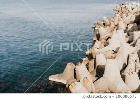 Coast breakwaters protecting from large waves with sea water background. The seashore is reinforced with concrete tetrapods. Coast breakwaters protecting from large waves with sea water background. The seashore is reinforced with concrete tetrapods. 100096575