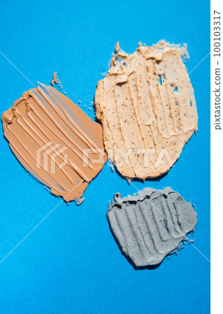 Different swatches of cosmetic products for the face and body on blue background. Texture of skin care cosmetic product. Vertical Different swatches of cosmetic products for the face and body on blue background. Texture of skin care cosmetic product. Vertical 100103317
