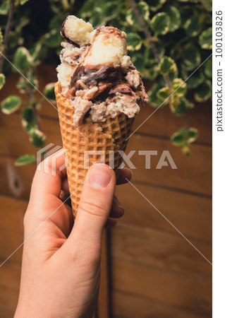 Female hand holding delicious american vanilla chocolate ice cream. Tasty homemade icecream Gelato in the waffle cone. Gluten free vegan dairy free Female hand holding delicious american vanilla chocolate ice cream. Tasty homemade icecream Gelato in the waffle cone. Gluten free vegan dairy free 100103826